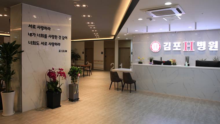 김포에이치H병원 — 대리석 질감의 벽면과 접수대가 있는 병원 로비에 한글 문구가 적힌 벽면과 화분들이 배치되어 있다