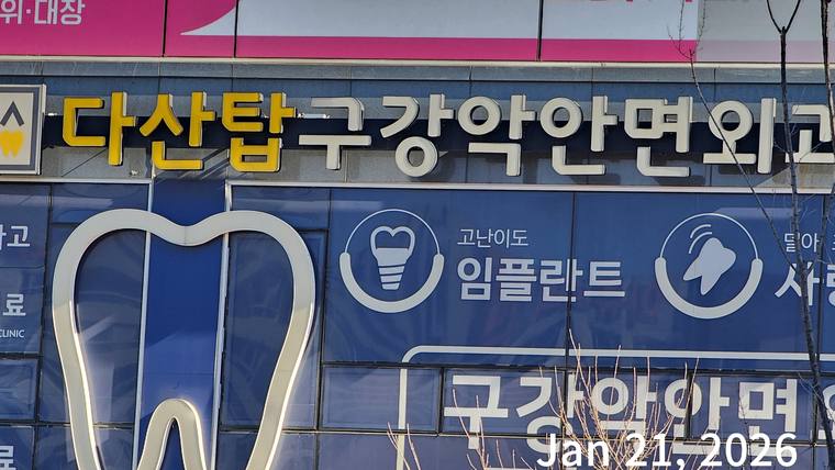 다산탑구강악안면외과치과의원 — 치과 병원의 간판과 임플란트 광고가 적힌 파란색 배경의 외벽이 촬영된 사진