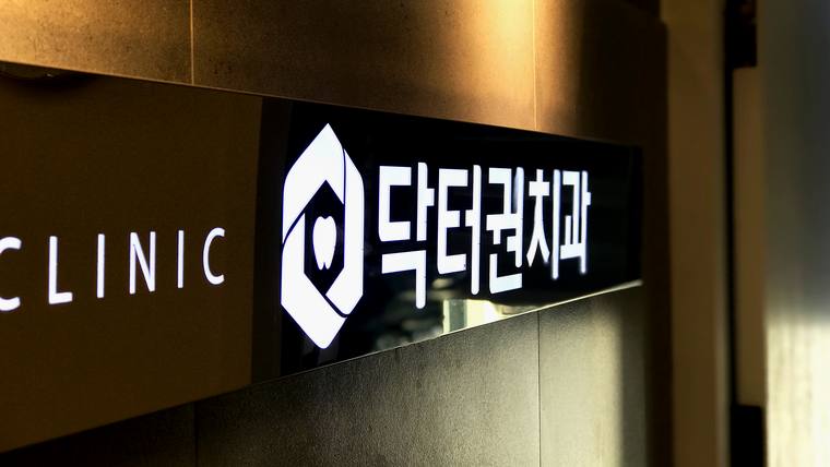 어두운 배경에 'CLINIC'과 '닥터권치과'라는 문구가 적힌 병원 간판이 촬영된 사진