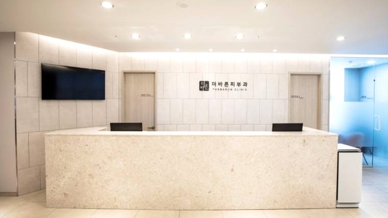 더바른피부과의원 — 대리석 질감의 긴 접수대가 있는 병원 로비의 내부 모습