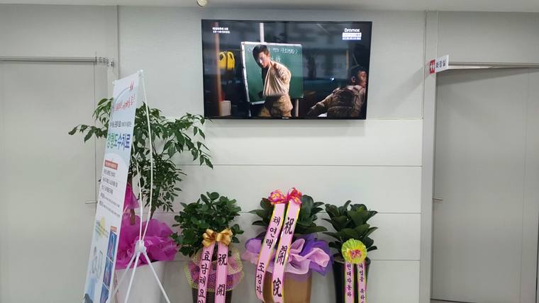 도화신경외과의원 — 병원 대기실 벽면에 TV 화면과 안내용 입간판, 그리고 화분들이 배치되어 있는 모습
