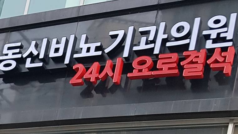 동신비뇨기과의원 — 검은색 바탕에 흰색과 빨간색 글씨로 병원 이름과 24시간 요로결석 진료 안내가 적힌 간판이다