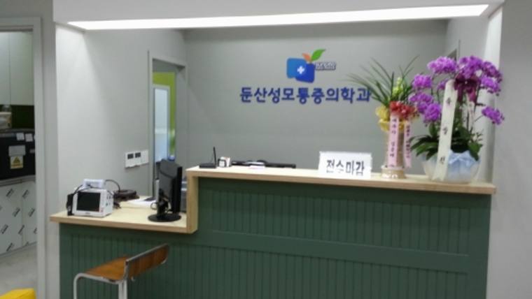 둔산성모마취통증의학과의원 — 병원이나 교육 기관의 접수대 위에 '동산성모통용의학교'라는 문구와 꽃 장식이 놓여 있는 실내 모습