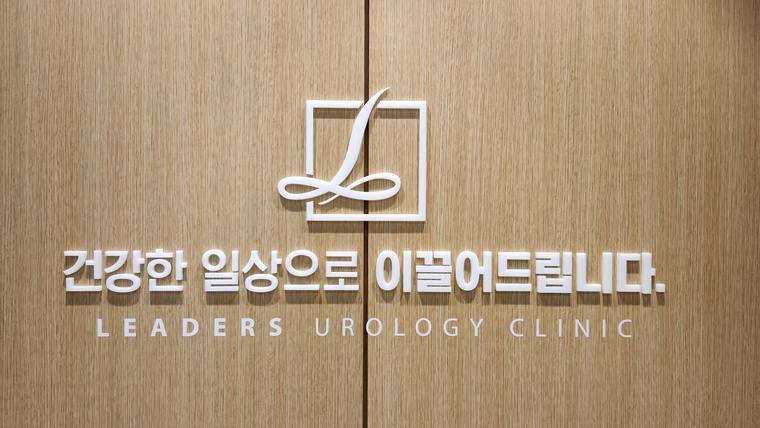 리더스비뇨의학과의원 — 나무 질감의 벽면에 병원 로고와 한글 및 영문 문구가 새겨진 간판이다