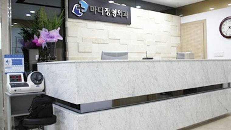 마디정형외과의원 — 대리석 느낌의 긴 접수대와 그 뒤로 한글이 적힌 간판이 있는 병원 내부 모습