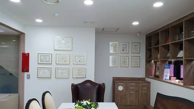 미인플란트치과의원 — 벽면에 여러 개의 증명서가 걸려 있고 소파와 가구가 배치된 병원 내부 대기실 공간이다