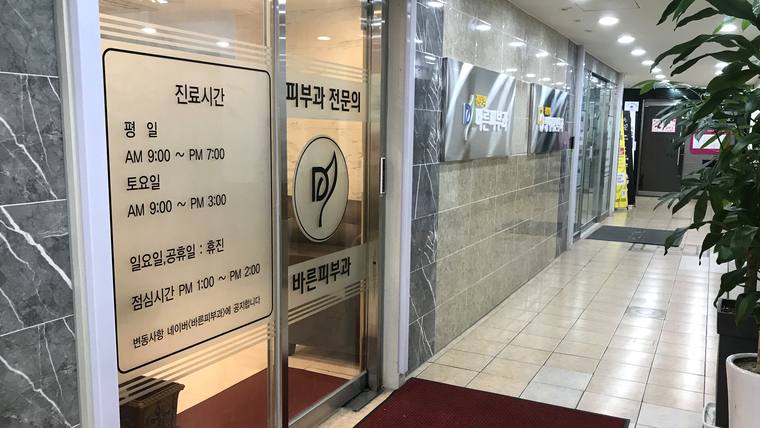 바른피부과의원 — 병원 입구의 유리문과 옆 벽면에 진료 시간 및 병원 명칭이 적힌 안내 문구가 보입니다