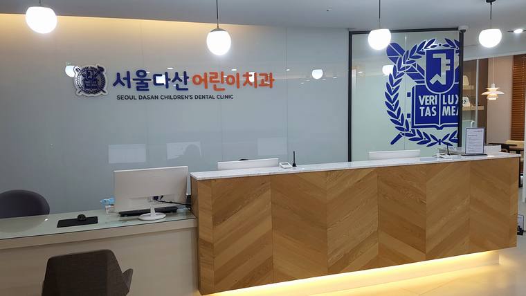 서울다산어린이치과의원 — 치과 병원의 접수대와 로고가 적힌 벽면이 보이는 내부 전경
