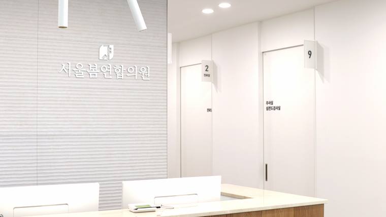 서울봄연합의원 — 흰색 벽면과 문이 있는 병원 내부 복도와 안내 문구가 적힌 벽면이 보입니다