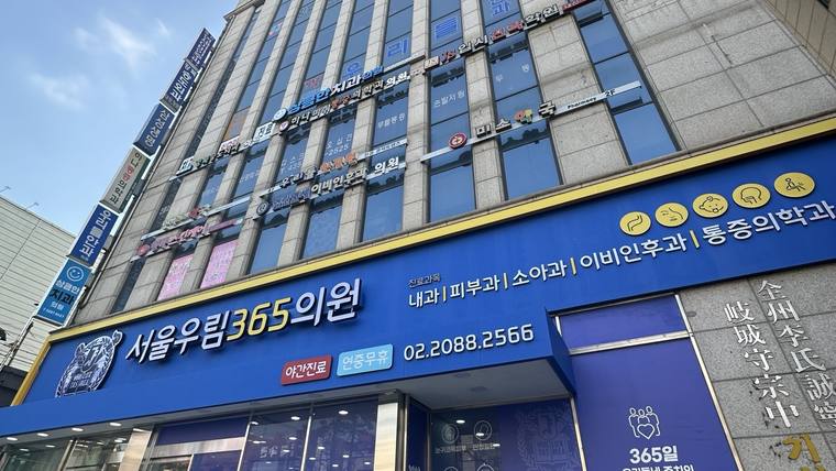 서울우림365의원 — 건물 외벽에 '서울의립365의원'이라는 문구와 여러 진료 과목이 적힌 파란색 간판이 크게 걸려 있