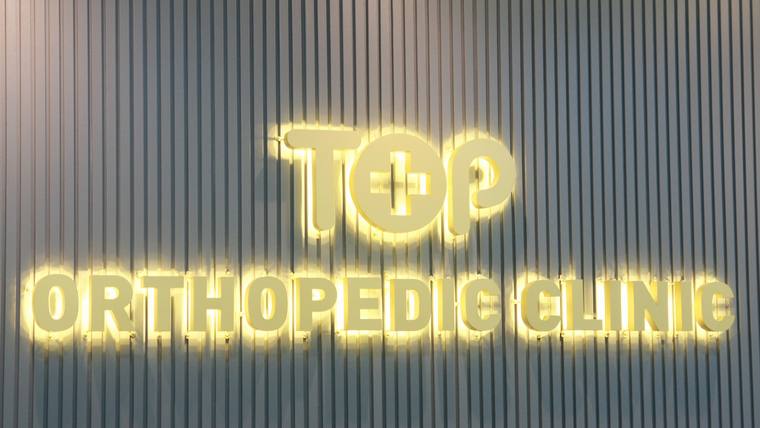 수완탑정형외과의원 — TOP Orthopedic Clinic이라는 문구가 적힌 노란색 조명의 병원 간판이 세로 줄무늬 벽면에 설치되어 있다