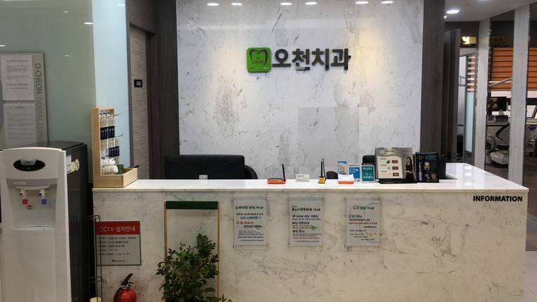 대리석으로 된 접수대 위에 안내문과 소독용품이 놓여 있고 배경에 '오천치과' 간판이 보입니다