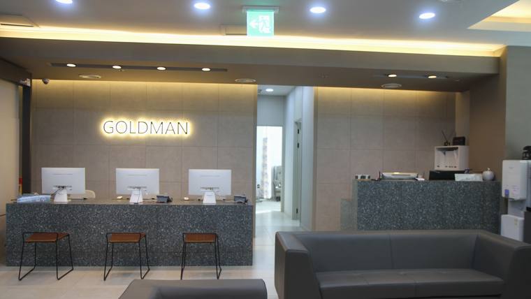 골드만비뇨기과의원 — GOLDMAN이라는 문구가 적힌 벽면 앞에 긴 접수대가 있고 그 앞에 의자들이 놓여 있는 실내 공간이다.