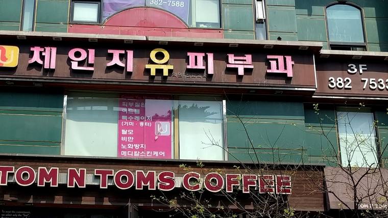 병원 건물 외벽에 '체인지유피부과'라는 간판과 홍보 내용이 적힌 포스터가 붙어 있고, 아래층에는 'TOM N TOMS COFFEE'라는 카페 간판이 보입니다.