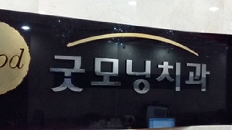 검은색 바탕에 금색 곡선과 흰색 글씨로 '굿모닝치과'라고 적힌 병원 간판이 보입니다