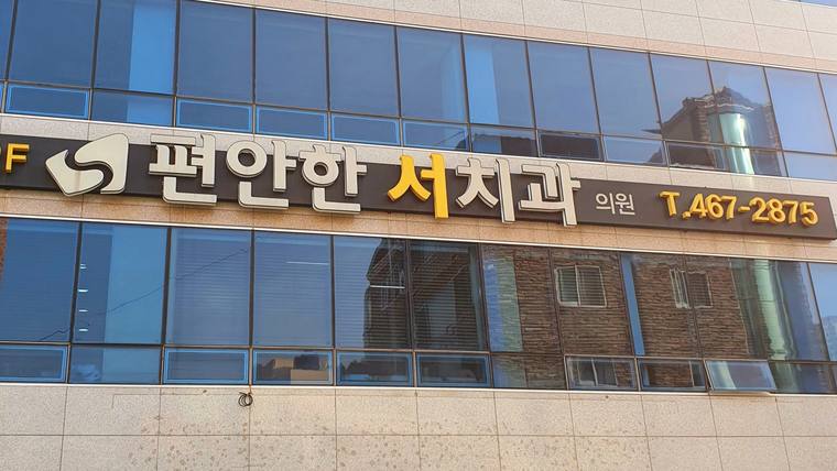 병원 건물 외벽에 '편안한 서치과'라는 문구와 전화번호가 적힌 간판이 부착되어 있다